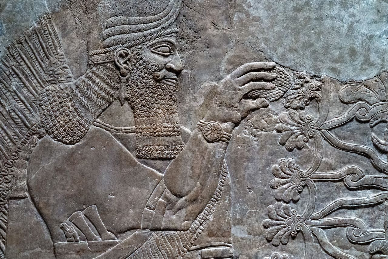 Assyrian stone relief of a bearded winged genius with a rosette bracelet, carved in fine detail on a gypsum panel from a Mesopotamian palace