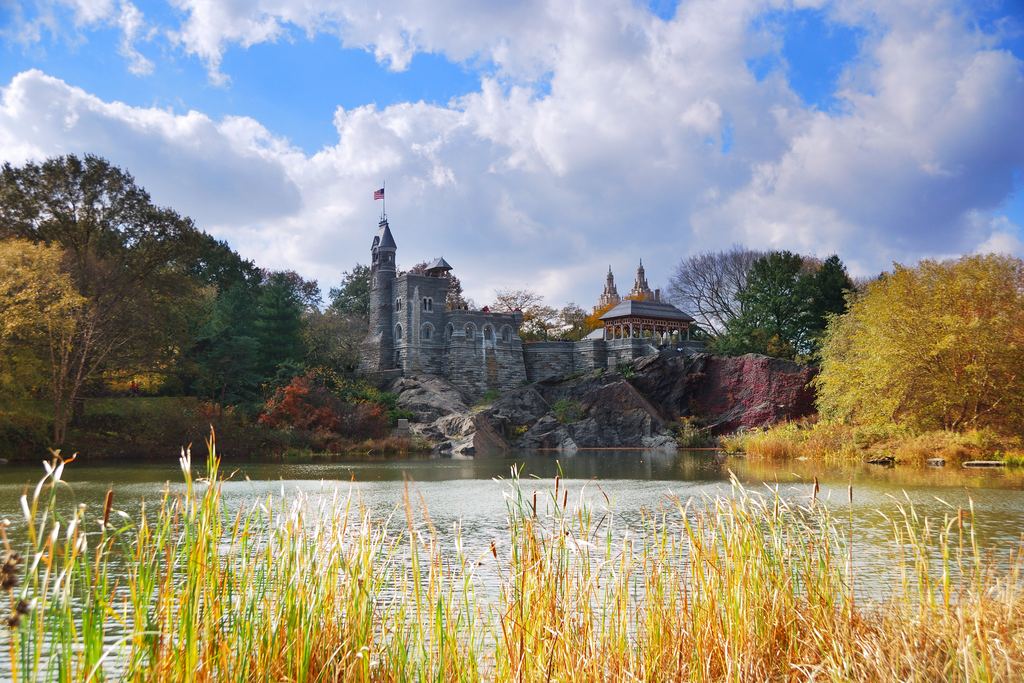 Belvedere Castle on Vista Rock in Central Park, seen across Turtle Pond with tall reeds and autumn trees under a blue sky