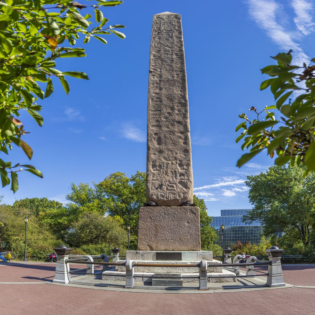 Cleopatra's Needle, the ancient Egyptian granite obelisk in Central Park just behind the Metropolitan Museum, on its railed plaza under a blue sky