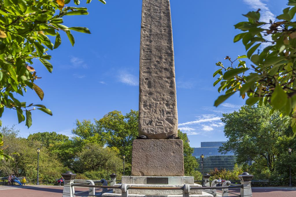 Cleopatra's Needle, the ancient Egyptian granite obelisk in Central Park just behind the Metropolitan Museum, on its railed plaza under a blue sky
