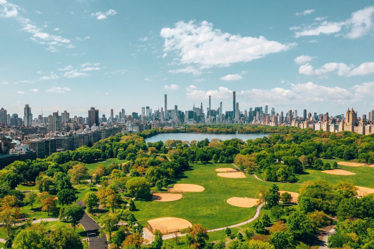 Aerial view of Central Park with the Great Lawn ball fields, the Reservoir and the Midtown Manhattan skyline beyond, framed by the buildings of the East and West Sides