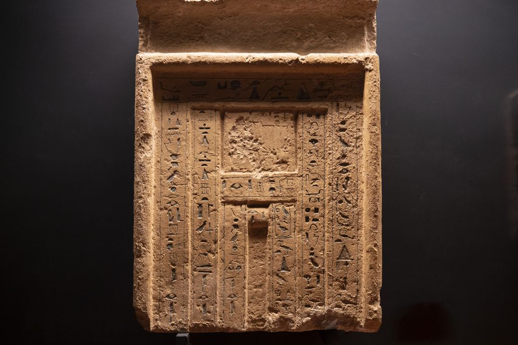 An ancient Egyptian limestone false door stela from the 6th Dynasty, carved with columns of hieroglyphs and lit against a dark museum background