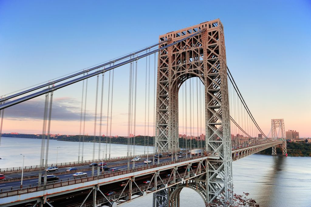 The steel tower of the George Washington Bridge over the Hudson River at dusk, with northern Manhattan beyond