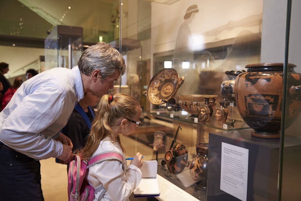 An older man and a young girl bending to look at ancient painted pottery in a museum display case