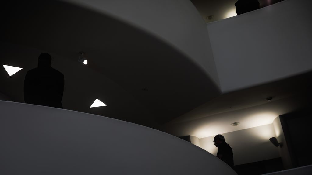 Silhouetted visitors on the curving spiral ramp inside the Solomon R. Guggenheim Museum in New York, with light falling on the white parapets