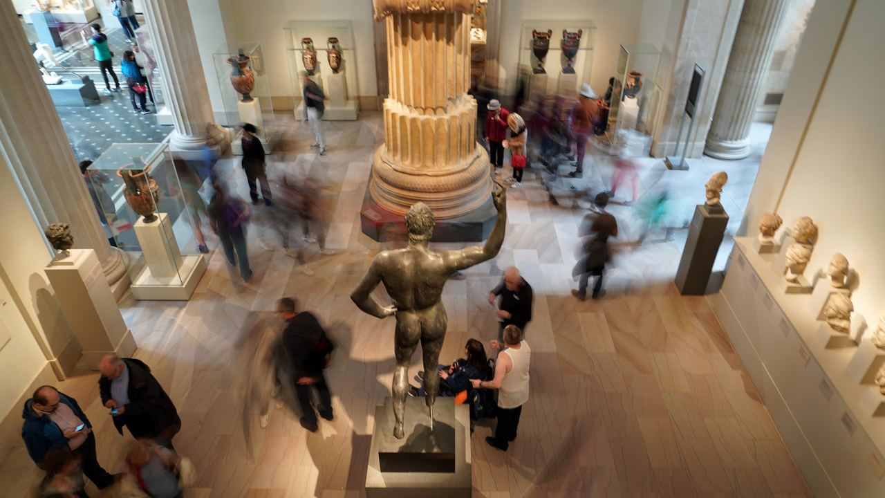 Visitors moving through the Greek and Roman galleries of the Metropolitan Museum in New York, seen from above, with the sculptures still