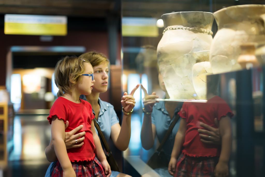 A mother and two young children looking at ancient vases in an illuminated museum display case
