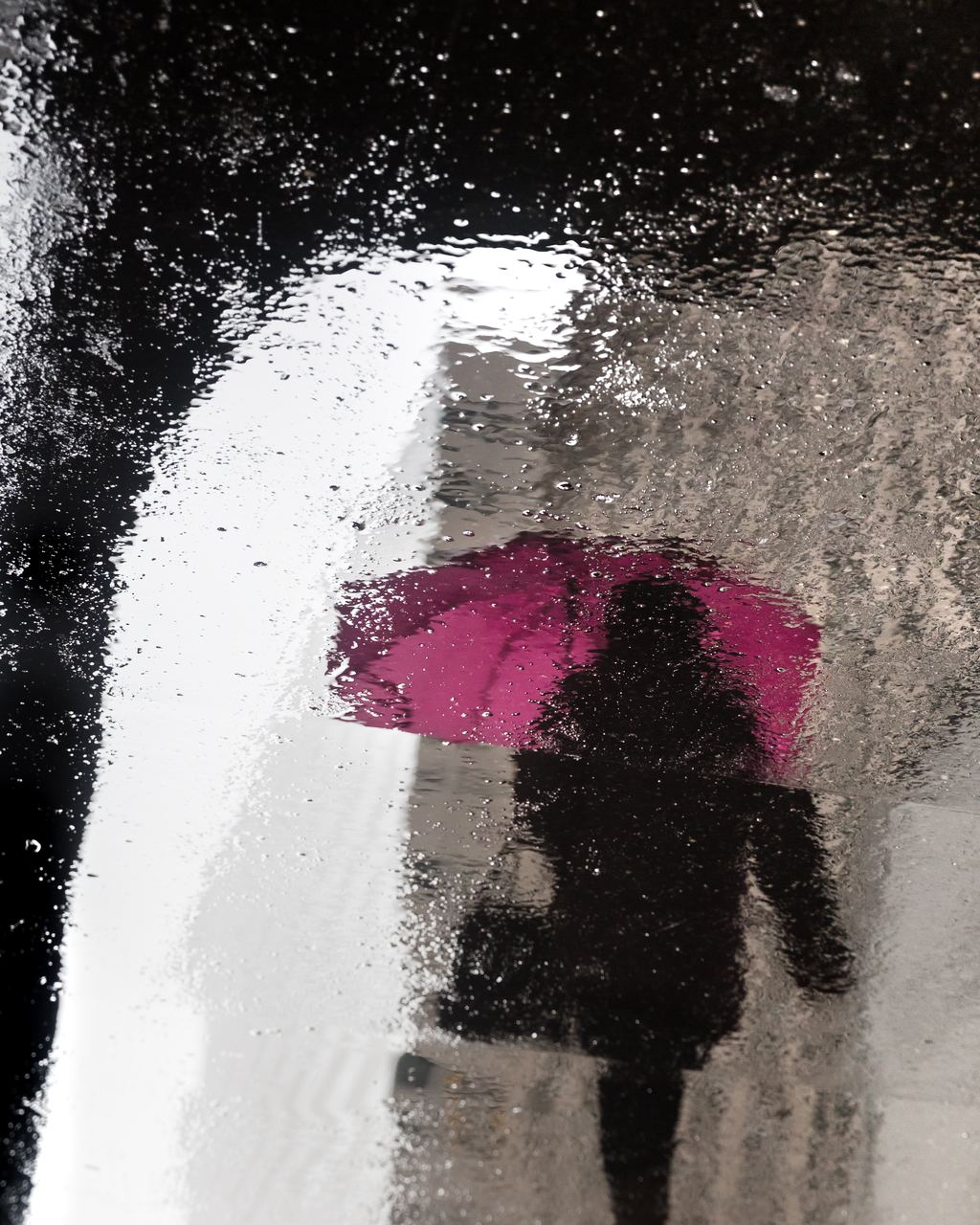 Reflection of a pedestrian with a pink umbrella on a wet New York sidewalk on a rainy day