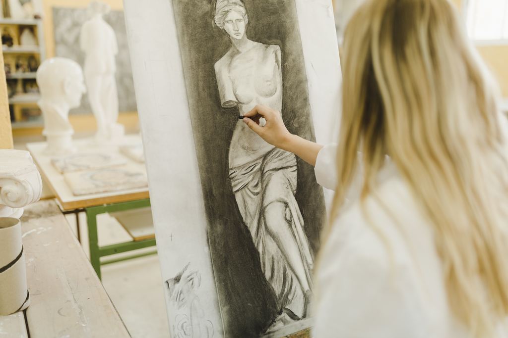A young woman sketching a classical sculpture in pencil on a large sheet of paper