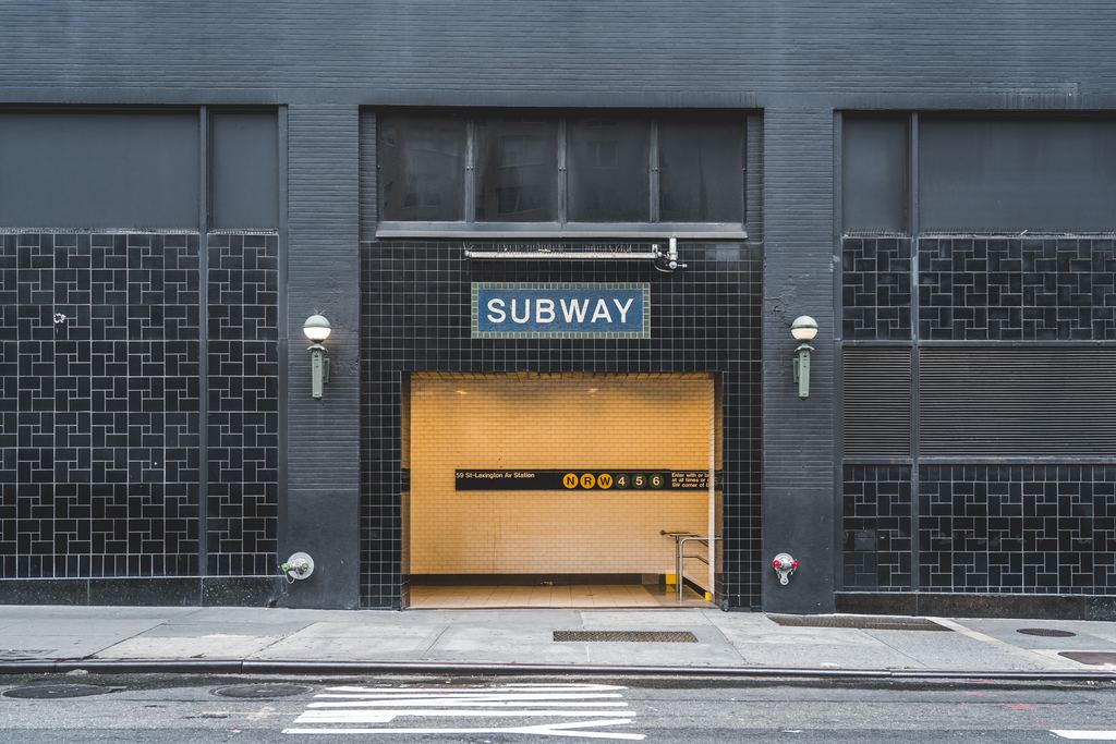 A subway entrance set into a building facade in New York, with the SUBWAY sign and green lamps either side