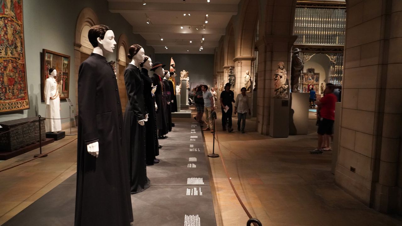 Visitors walking down a long medieval gallery of the Metropolitan Museum of Art past tapestries and display cases, New York