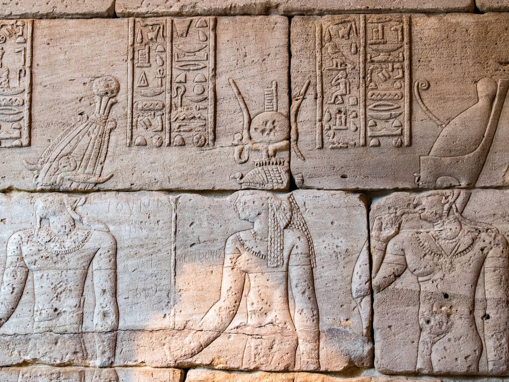 Sandstone wall of the Temple of Dendur at the Metropolitan Museum, carved with hieroglyphs and relief figures of gods and a king, in warm raking light