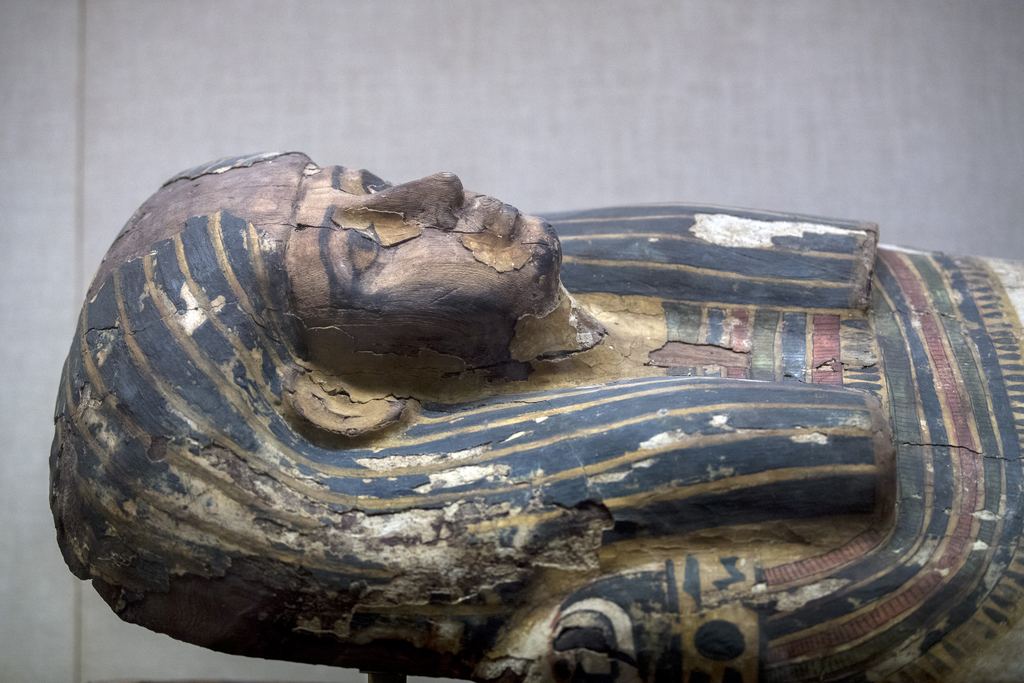 A blue and gold striped ancient Egyptian coffin lid lying in a display case at the Metropolitan Museum, New York