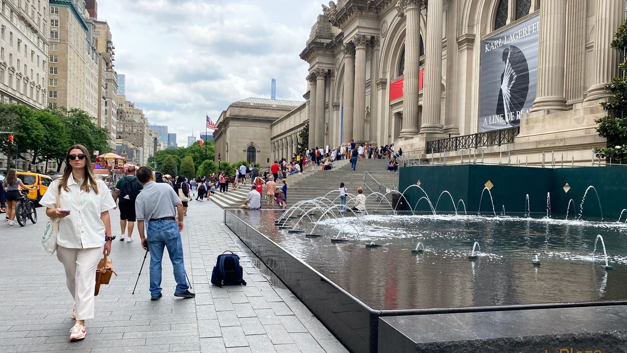 The Beaux-Arts facade of the Metropolitan Museum of Art on Fifth Avenue, with the fountains of David H. Koch Plaza and people on the sidewalk