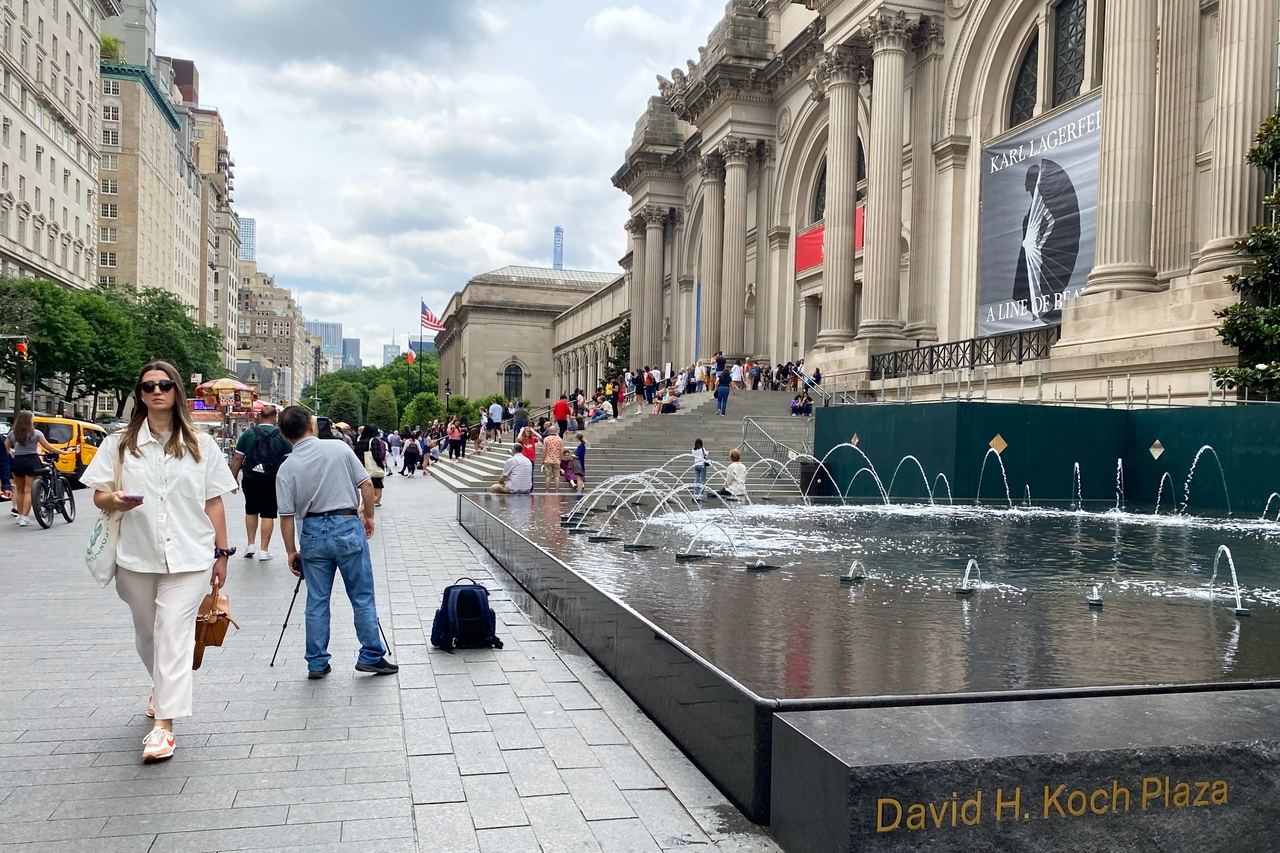The Beaux-Arts facade of the Metropolitan Museum of Art on Fifth Avenue, with the fountains of David H. Koch Plaza and people on the sidewalk