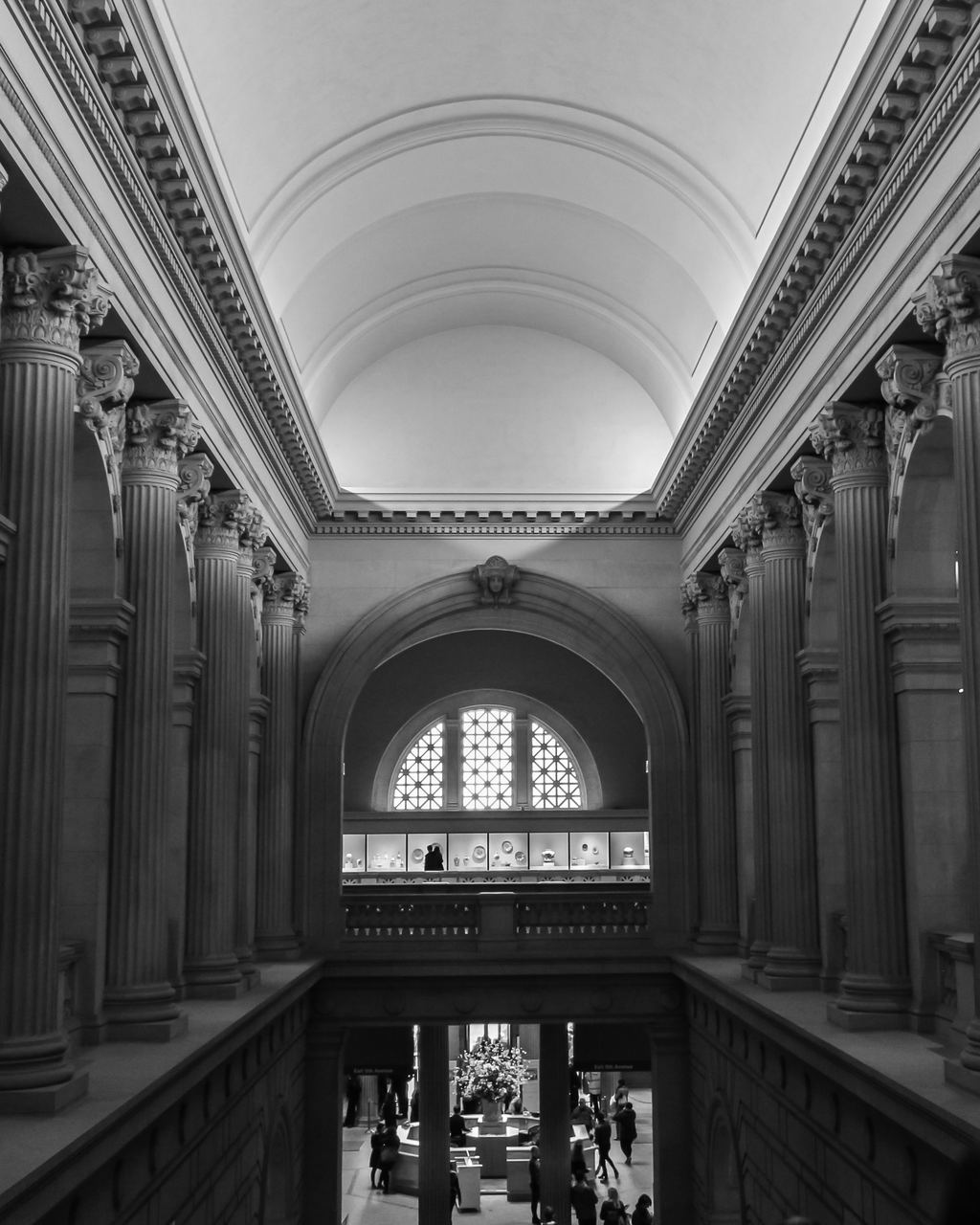Black-and-white view along the Great Hall balcony of the Metropolitan Museum of Art, with paired columns, a coffered vault and the entrance floor below