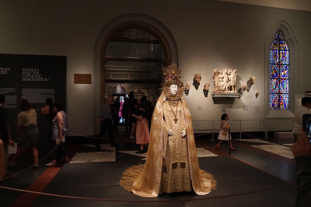 A medieval gallery of the Metropolitan Museum of Art with a stained-glass window, carved sculptures and a gilded vestment on display in 2018