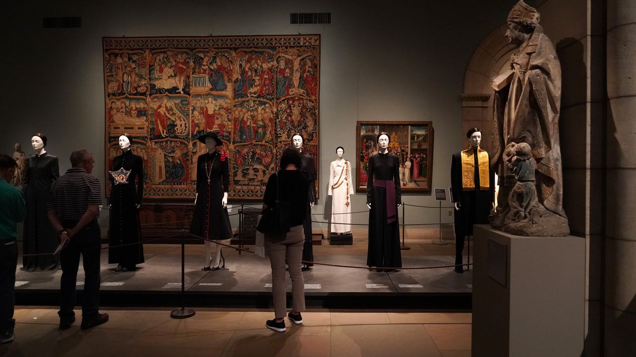 Visitors in a medieval gallery of the Metropolitan Museum of Art with a large tapestry and a carved stone saint, New York