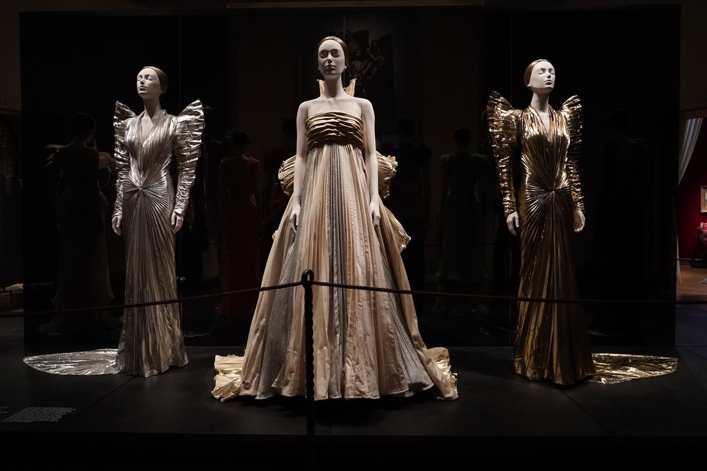 Three couture gowns spot-lit in a dark gallery during the Costume Institute's 2018 exhibition at the Metropolitan Museum