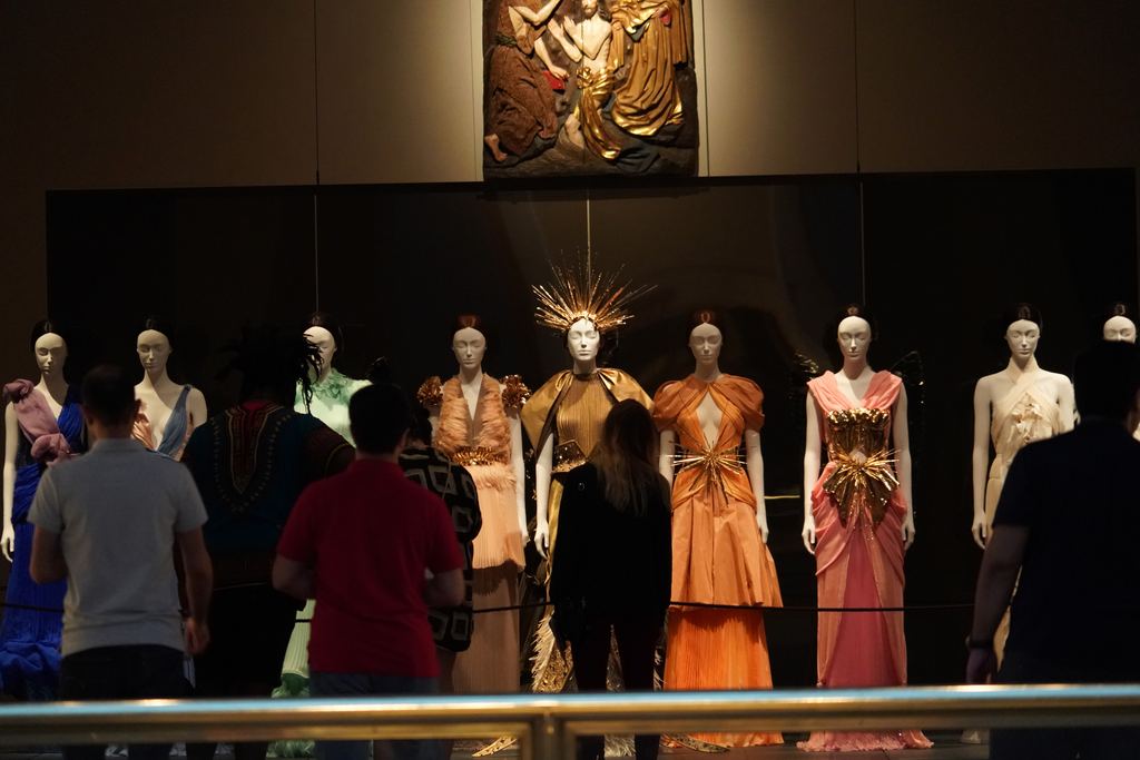 Visitors viewing a row of gowns on display during the 2018 Heavenly Bodies exhibition at the Metropolitan Museum of Art, New York