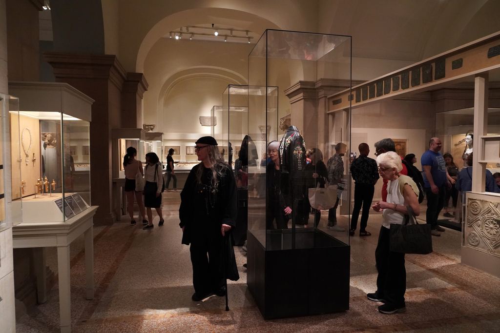 Visitors browsing display cases in a vaulted medieval gallery of the Metropolitan Museum of Art during the 2018 Heavenly Bodies exhibition