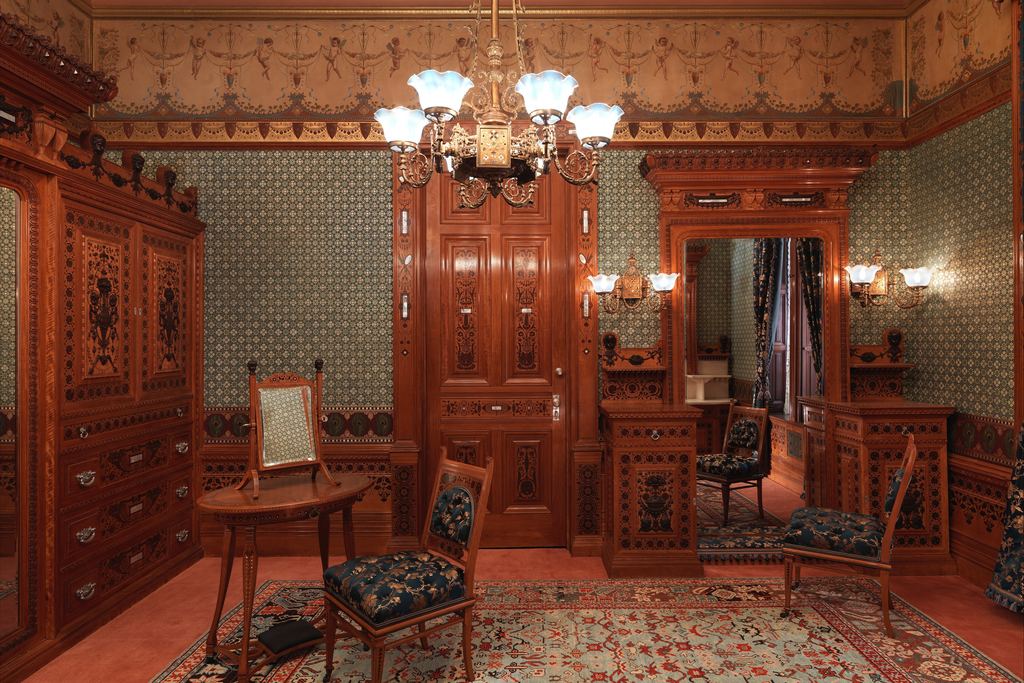 The Worsham-Rockefeller Dressing Room at the Metropolitan Museum: inlaid wood cabinetry, patterned blue wallpaper, a painted frieze, a gas chandelier and upholstered chairs on a Persian-style carpet