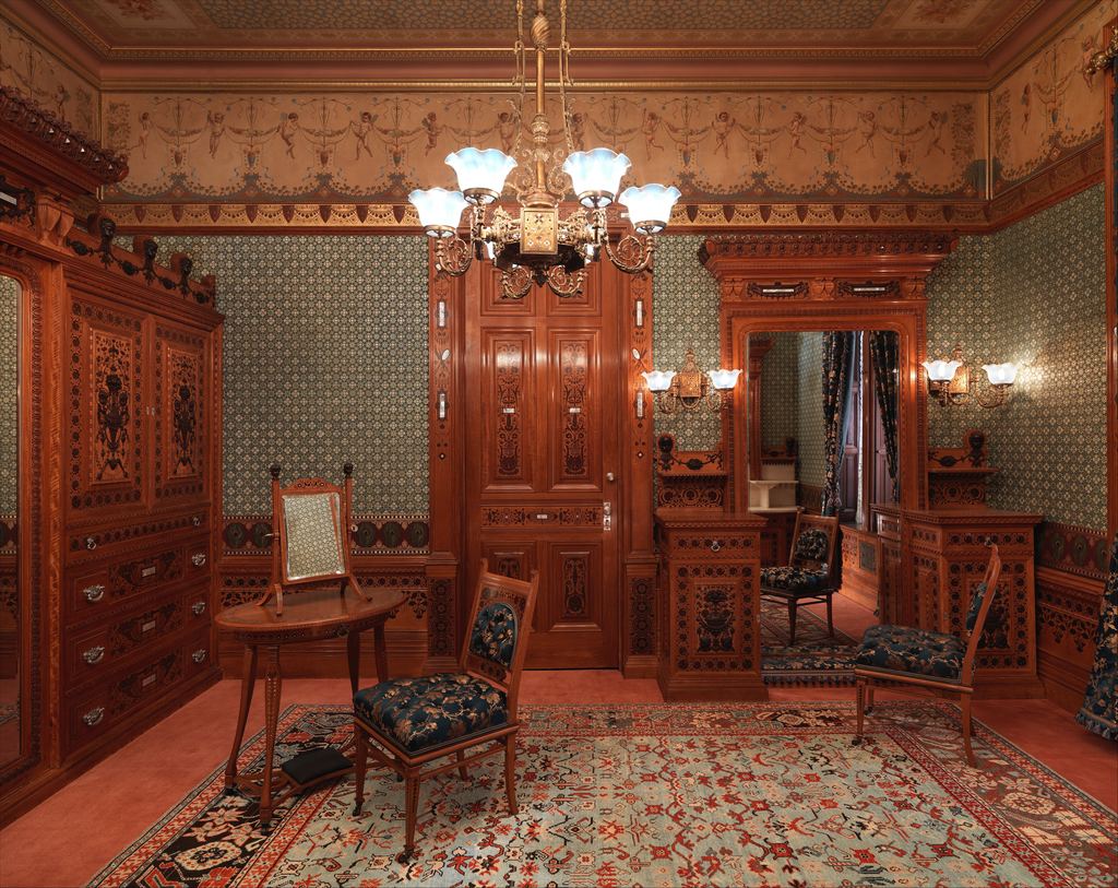 The Worsham-Rockefeller Dressing Room at the Metropolitan Museum: inlaid wood cabinetry, patterned blue wallpaper, a painted frieze, a gas chandelier and upholstered chairs on a Persian-style carpet