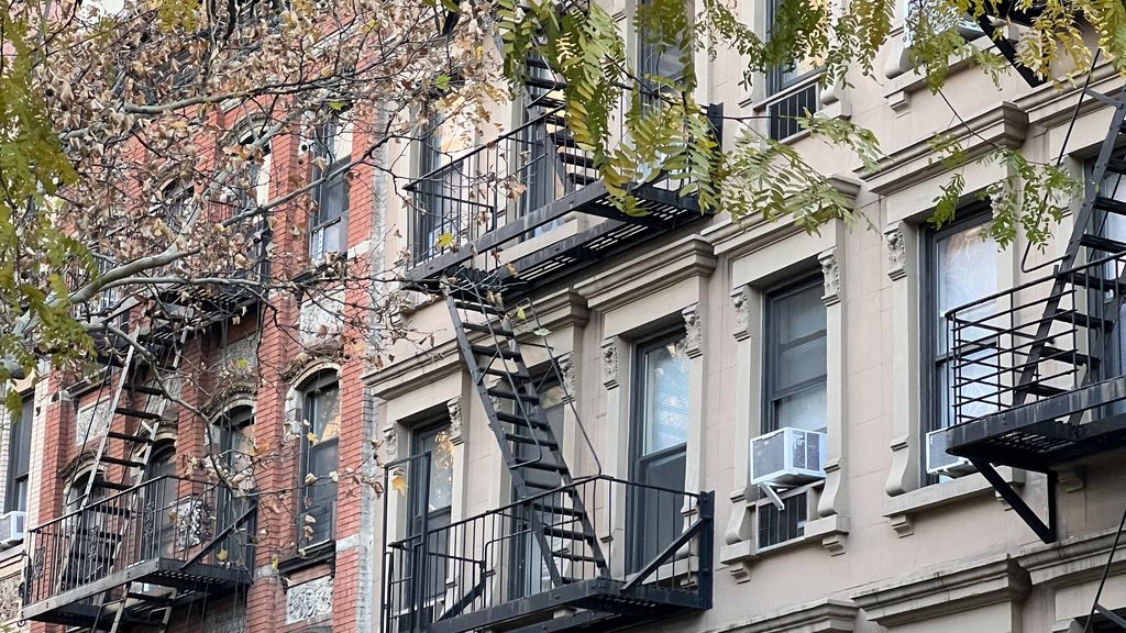 Nineteenth-century row houses with fire escapes and street trees on a side street of the Upper East Side, near Fifth Avenue