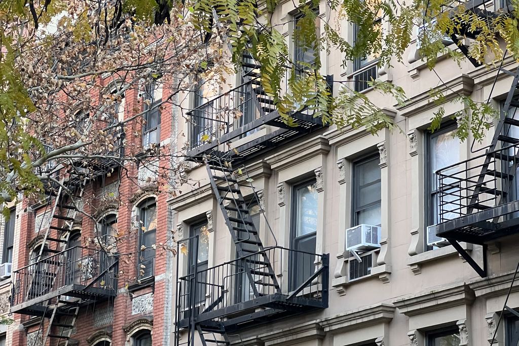 Nineteenth-century row houses with fire escapes and street trees on a side street of Manhattan's Upper East Side