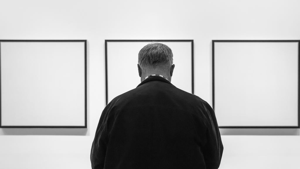 A visitor seen from behind looking at framed works on a white wall inside the Museum of Modern Art, New York