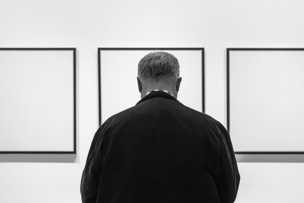 A visitor seen from behind looking at framed works on a white wall inside the Museum of Modern Art, New York