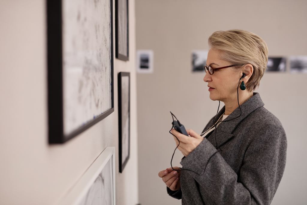 A visitor listening to an audio guide on earphones while studying framed drawings in a museum gallery