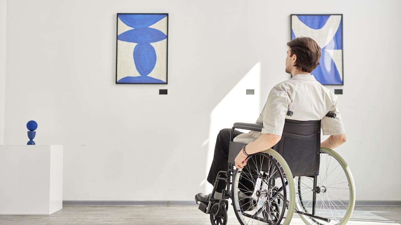 A man in a wheelchair looking at framed prints in a bright, step-free art gallery